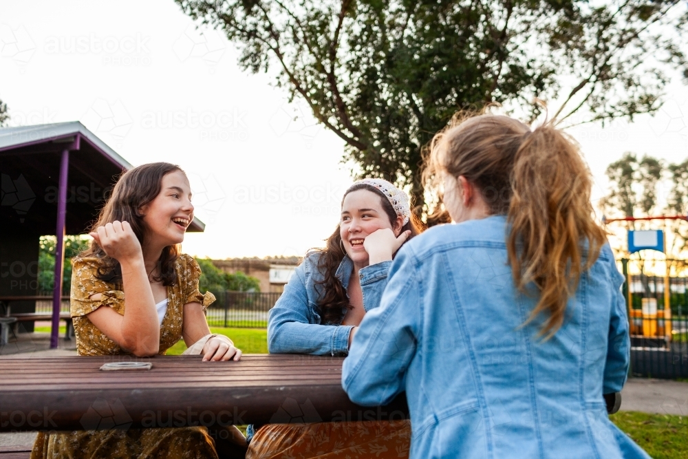 Group of teen friends chatting together having a conversation around park bench - Australian Stock Image