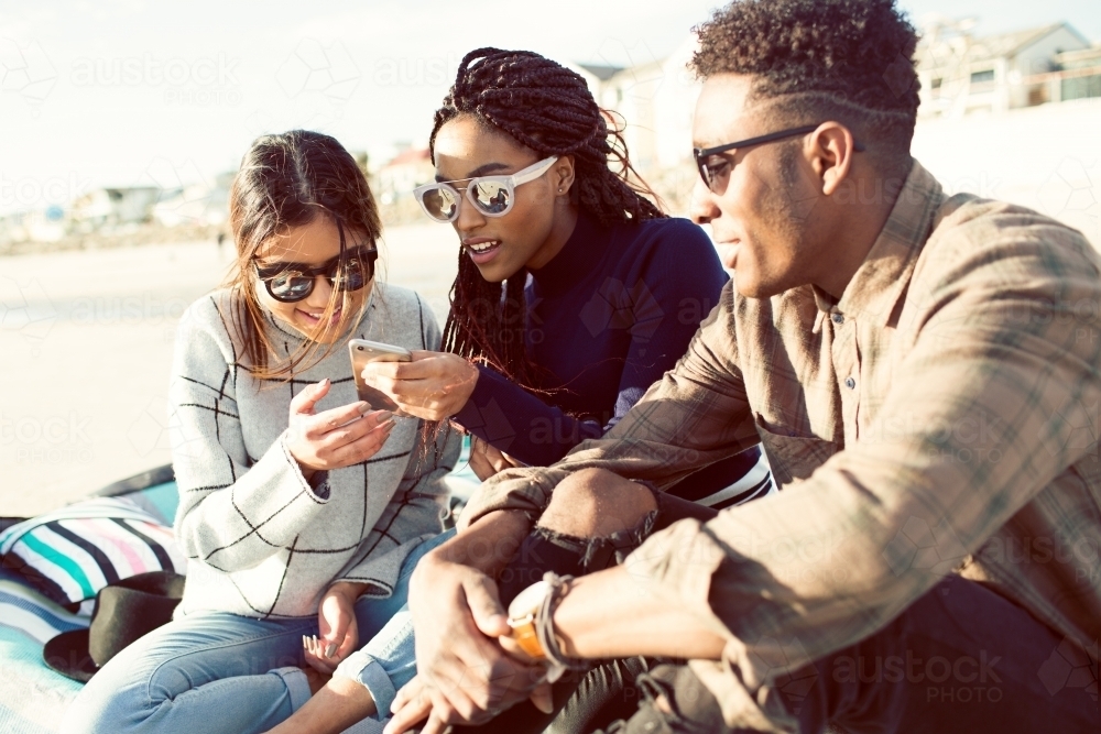 Group of teenage friends looking at a phone outdoors - Australian Stock Image
