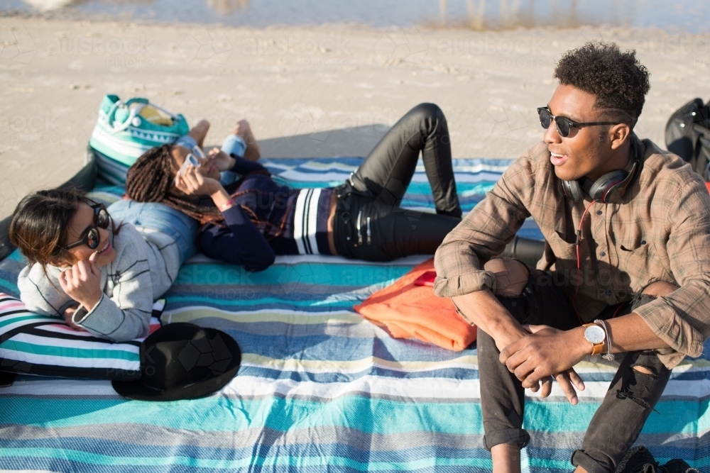 Group of teenagers sitting on a picnic rug at the beach - Australian Stock Image