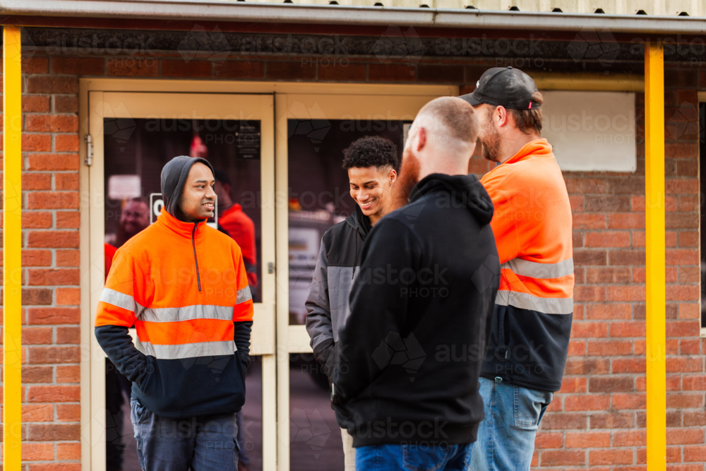 Group of workmen mechanics chatting together outside office at workplace some in high-vis - Australian Stock Image