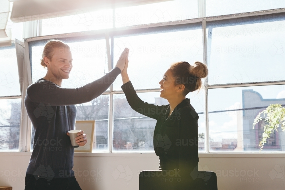 Guy and girl doing a high five to celebrate in an office - Australian Stock Image