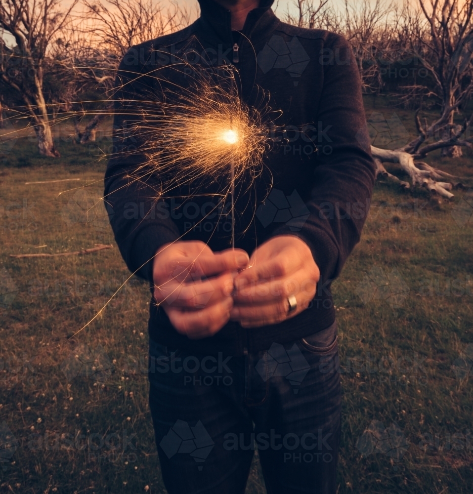 Guy holding a sparkler to camera on a mountain top at dusk - Australian Stock Image