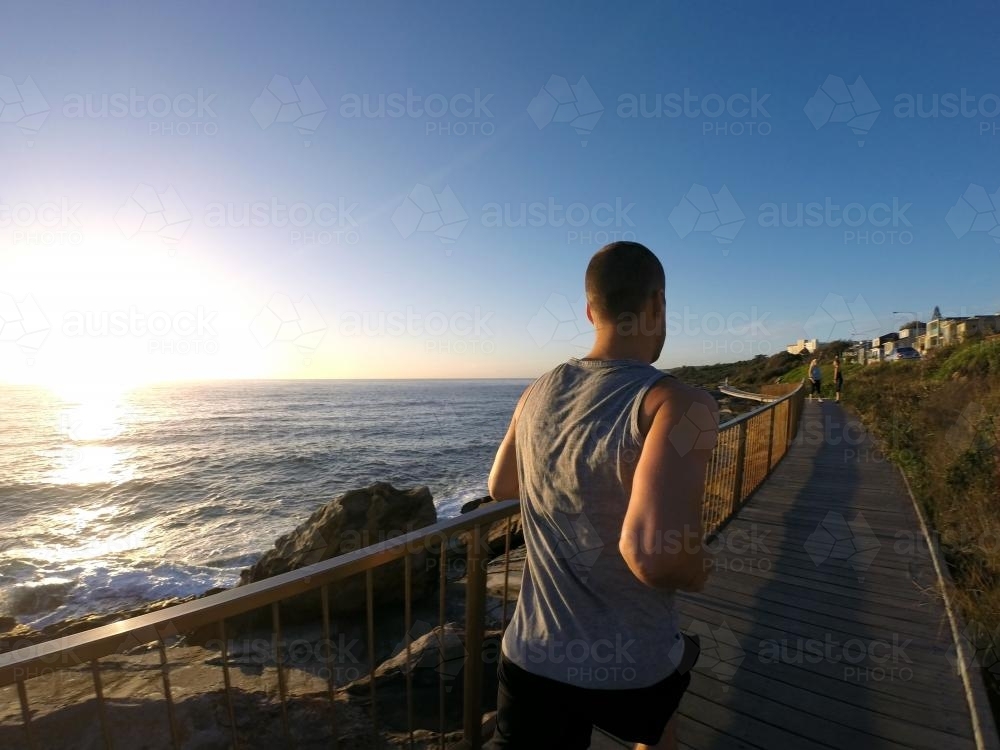 Guy jogging near ocean at sunrise - Australian Stock Image