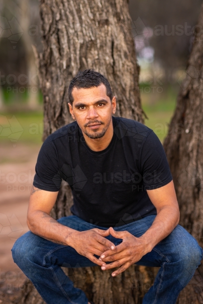 guy outdoors casually squatting in front of tree - Australian Stock Image