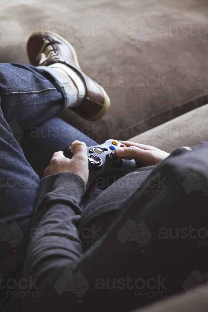 Guy using game controller on couch with space for text - Australian Stock Image