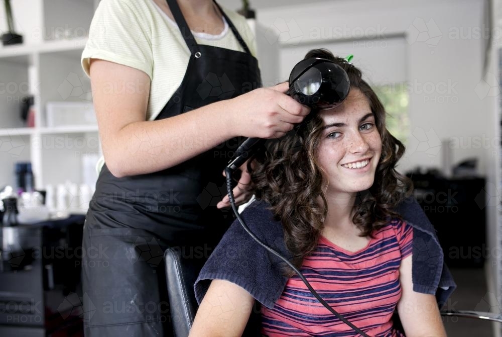 Hairdresser curling a young woman's hair - Australian Stock Image