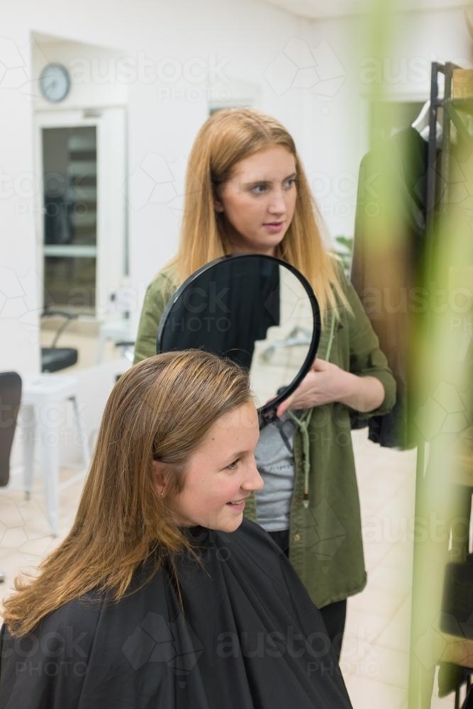 hairdresser showing teenage client her hair style with a small mirror - Australian Stock Image