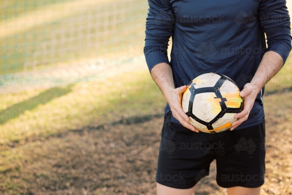 half body shot of a man holding a soccer ball while standing on the field - Australian Stock Image
