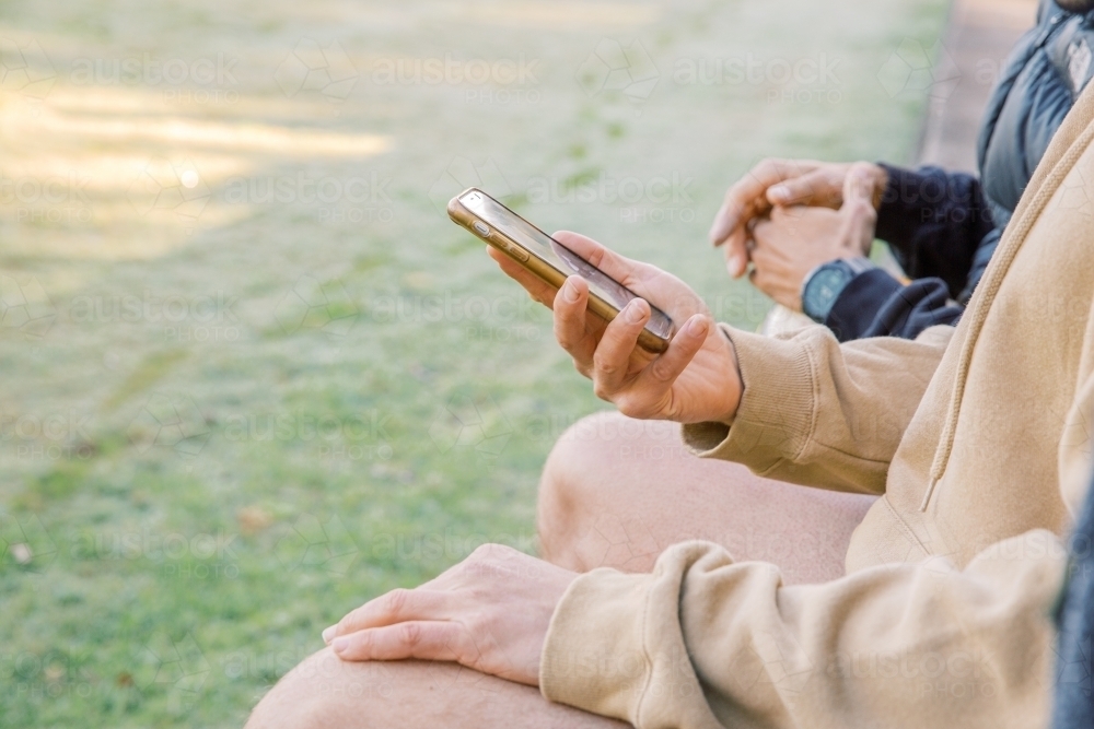 Half body shot of a man holding his cellphone wile sitting with a friend on his side - Australian Stock Image