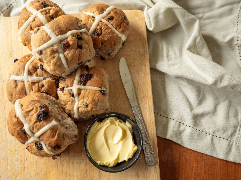 Half dozen Hot Cross Buns on wooden cutting board with butter and knife and linen napkin - Australian Stock Image