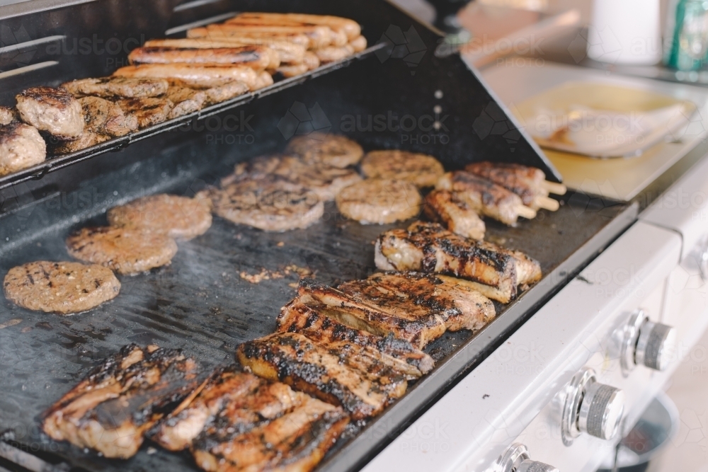 Hamburger patties and sausages cooking on a bbq, with some smoke rising from the hotplate - Australian Stock Image