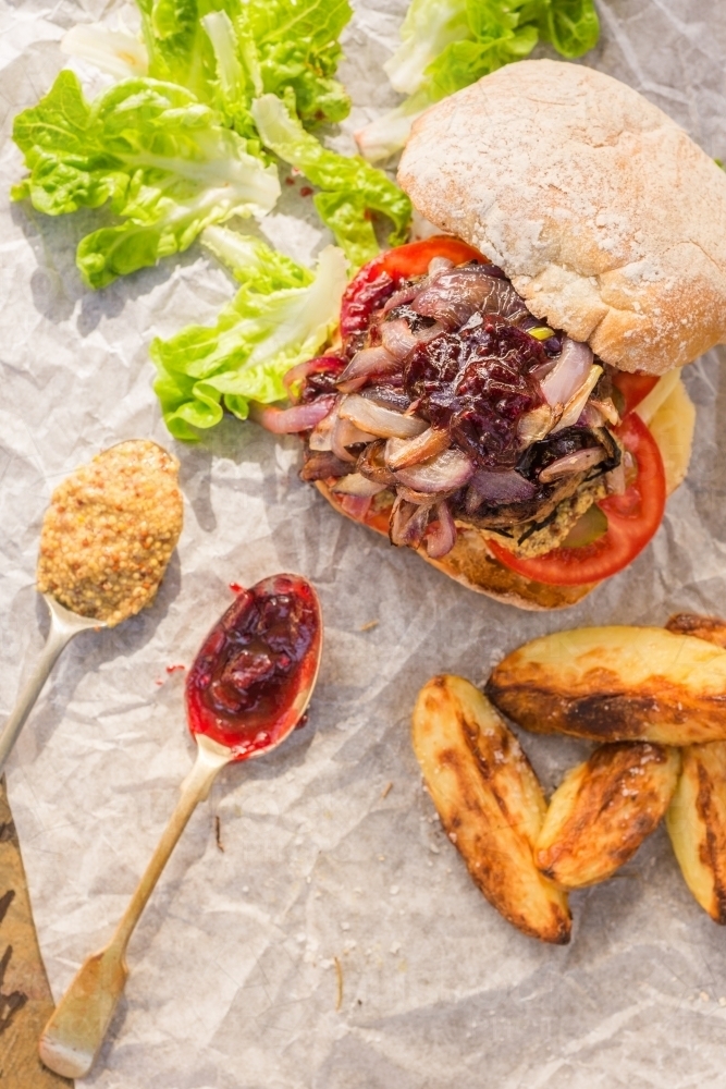 hamburger with potato wedges and two spoons with mustard and relish - Australian Stock Image