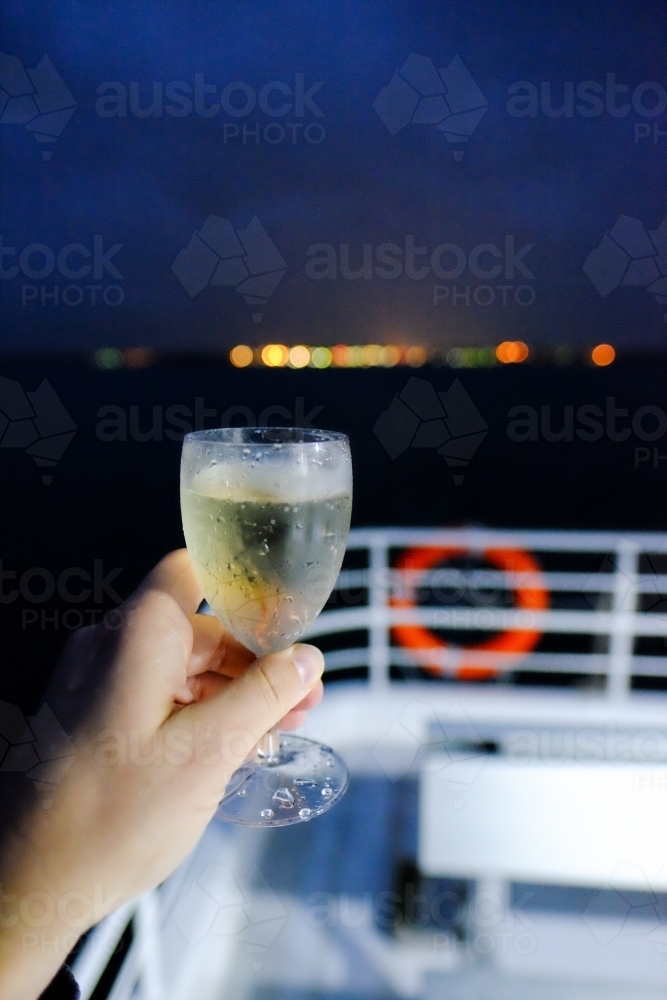 Hand holding a glass of white wine on a boat at night - Australian Stock Image