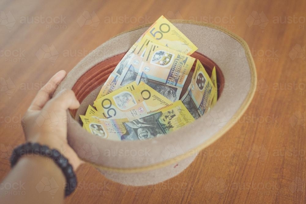 Hand holding fifty dollar notes in a hat - Australian Stock Image
