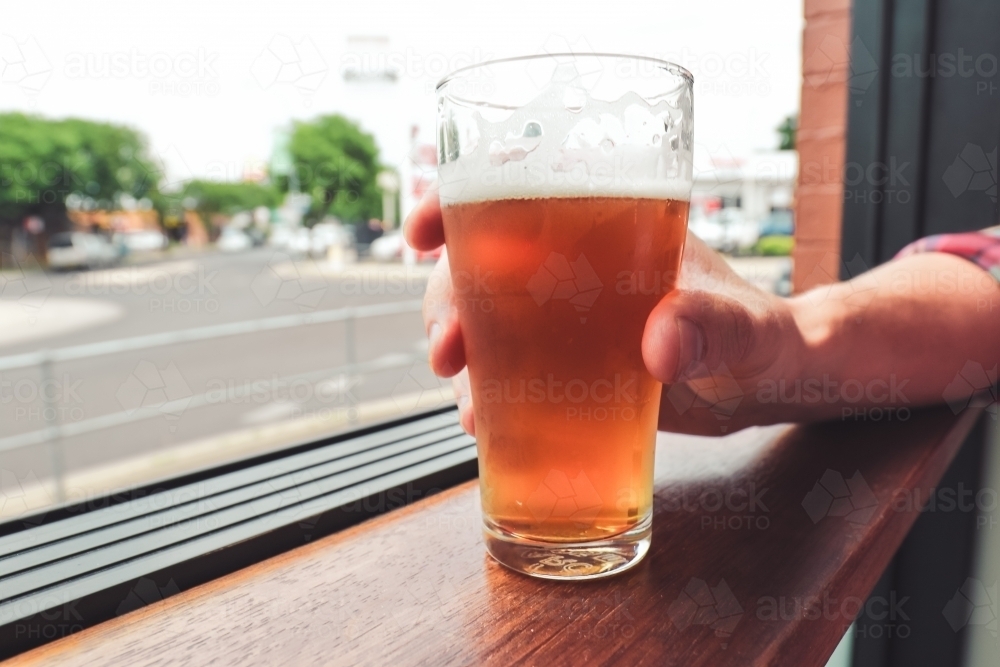 Hand holding glass of craft beer on window ledge over looking a street - Australian Stock Image