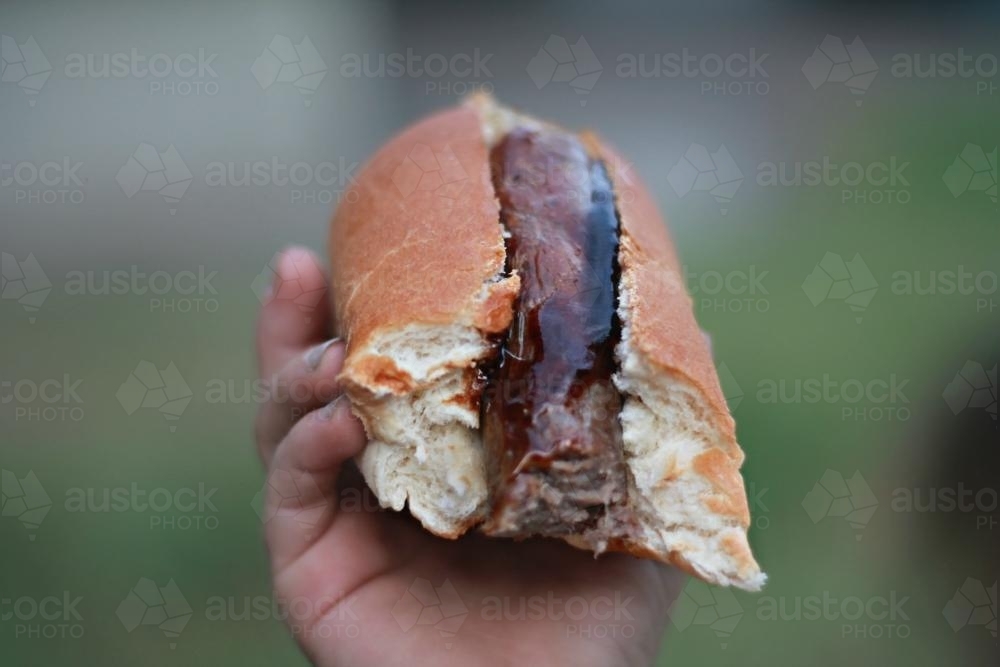 Hand holding hot dog sausage in bread - Australian Stock Image