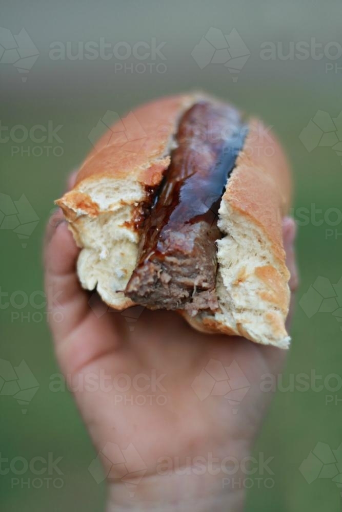 Hand holding hot dog sausage in bread - Australian Stock Image