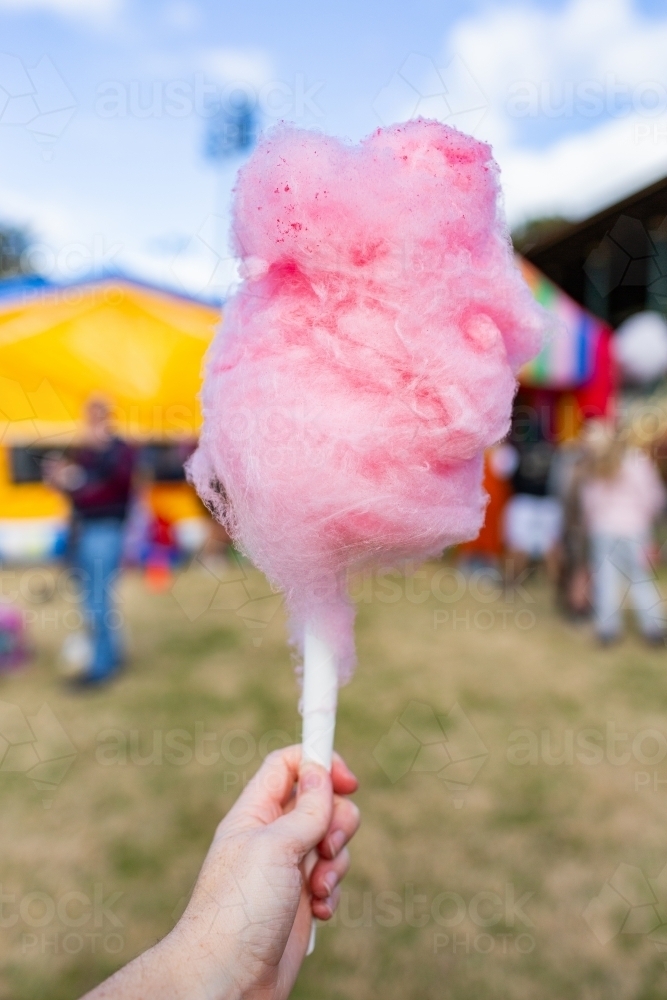Hand holding pink cotton candy at colourful fair event - Australian Stock Image