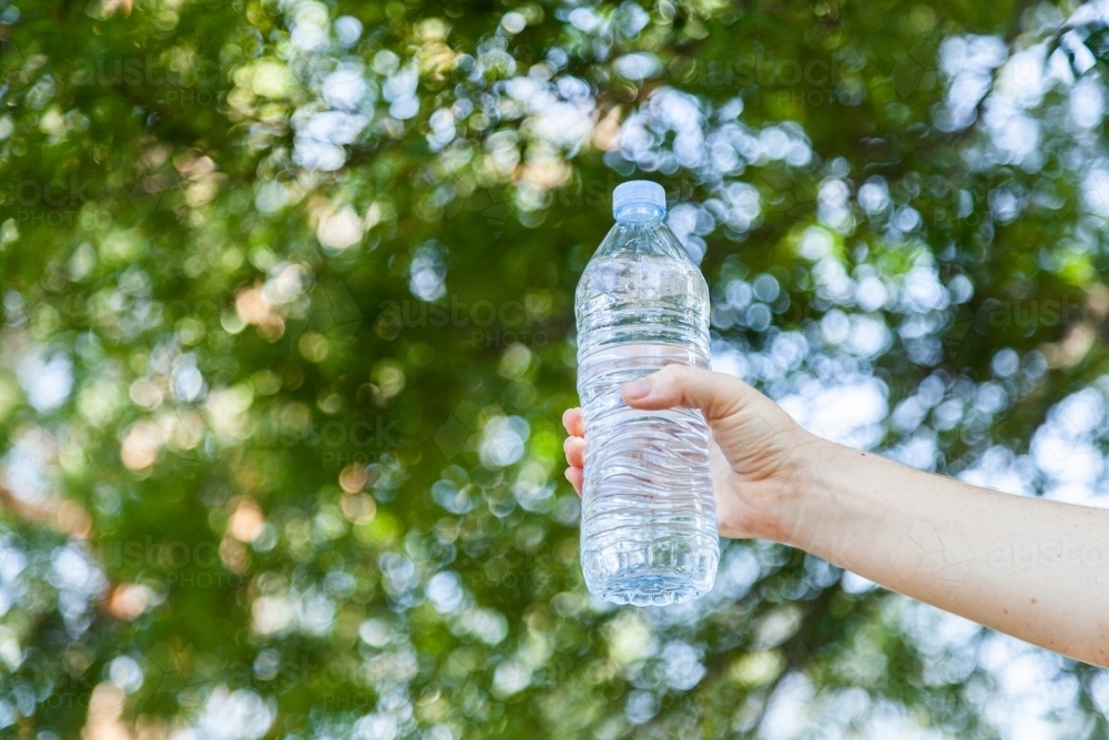Image of hand holding plastic water bottle outside with bokeh copy space Austockphoto