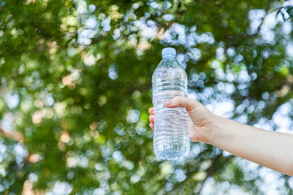 hand holding plastic water bottle outside with bokeh copy space - Australian Stock Image