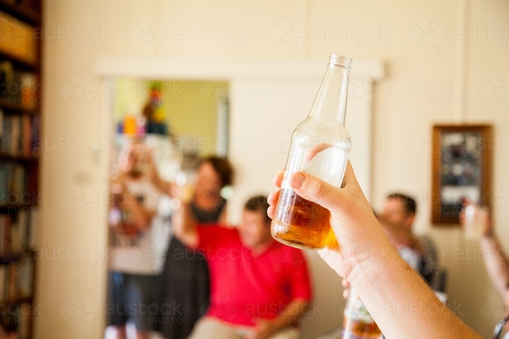 Hand holding up a bottle of beer for a toast at family gathering - Australian Stock Image