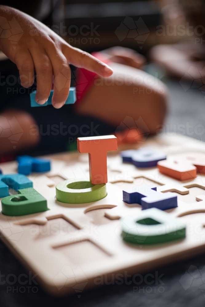 hand of Aboriginal boy playing with alphabet letter puzzle pieces - Australian Stock Image
