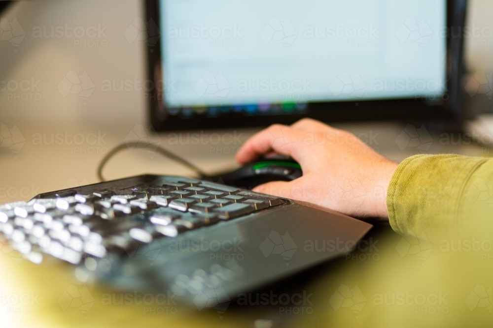 Hand on mouse beside computer keyboard - Australian Stock Image