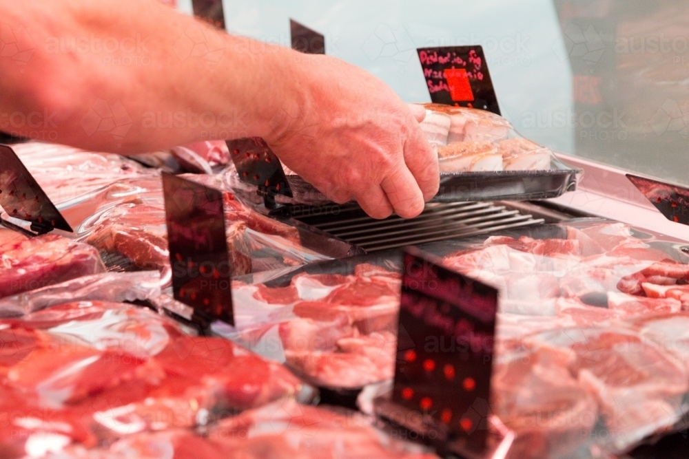 Hand placing meat on counter at butcher - Australian Stock Image