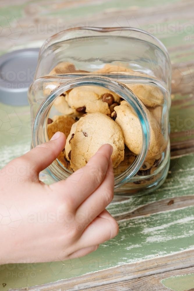hand reaching for choc chip cookies in a glass cookie jar - Australian Stock Image