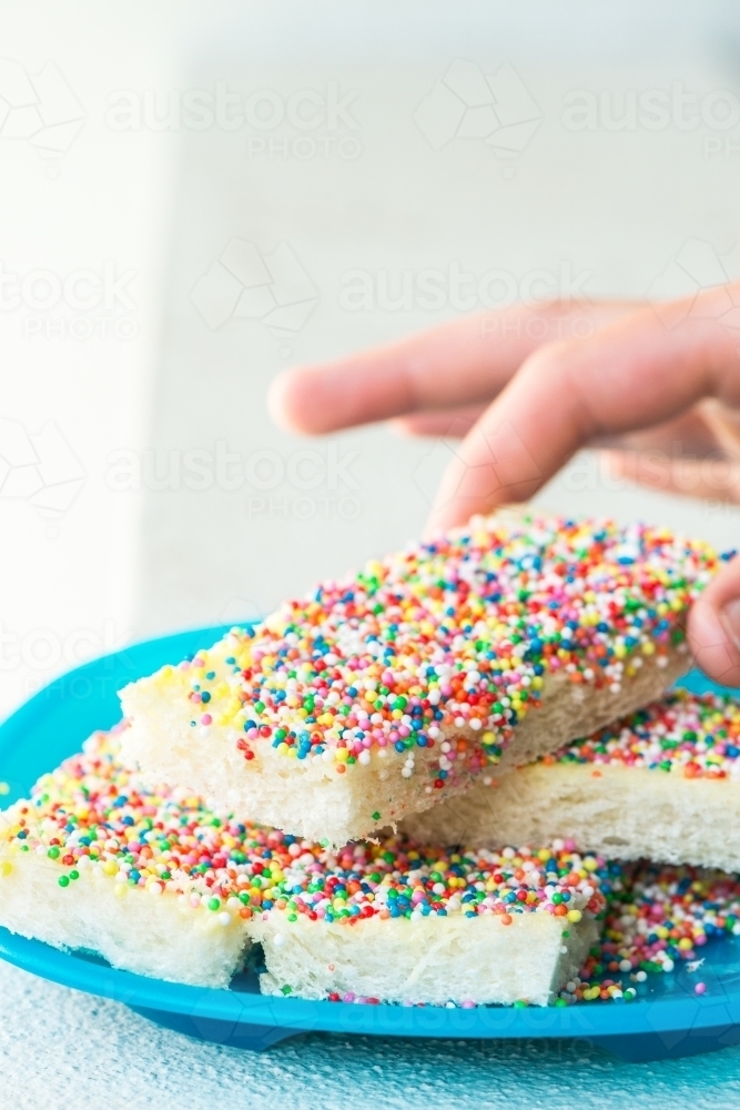 Hand reaching for fairy bread on a plate - Australian Stock Image