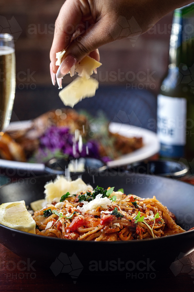hand sprinkles grated cheese over a plate of pasta - Australian Stock Image
