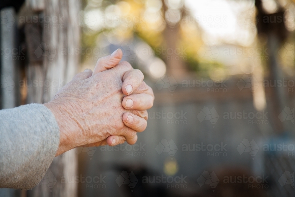 Hands clasped together as lady farmer leans on fence - Australian Stock Image
