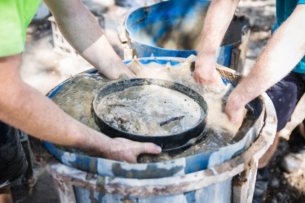 Hands in muddy water of fossicking drum holding sieve - Australian Stock Image