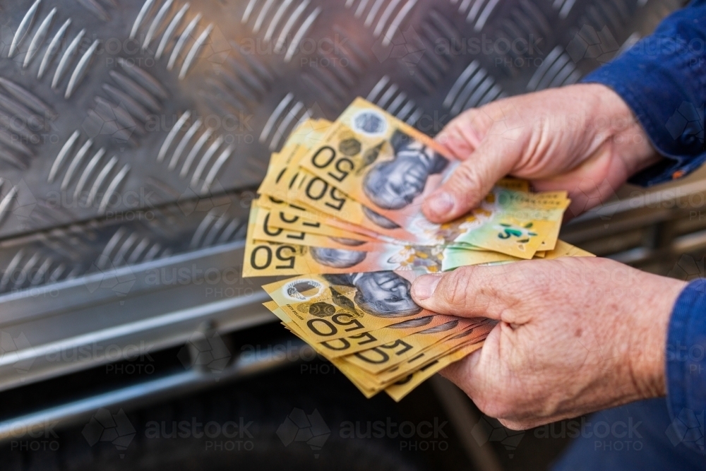 Hands of a handyman counting cash beside tradie ute - Australian Stock Image