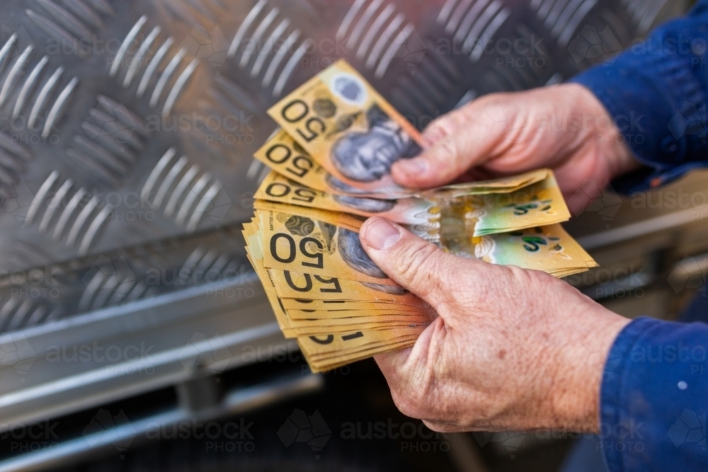 Hands of a handyman counting cash beside tradie ute - Australian Stock Image
