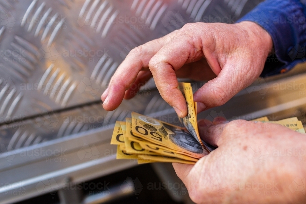 Hands of a handyman counting cash beside tradie ute - Australian Stock Image