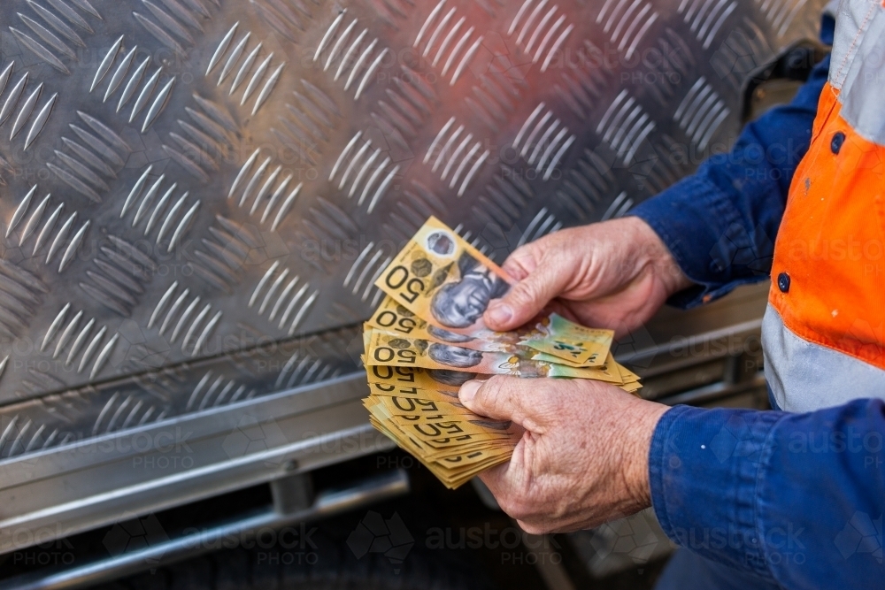 Hands of a handyman counting cash beside tradie ute - Australian Stock Image