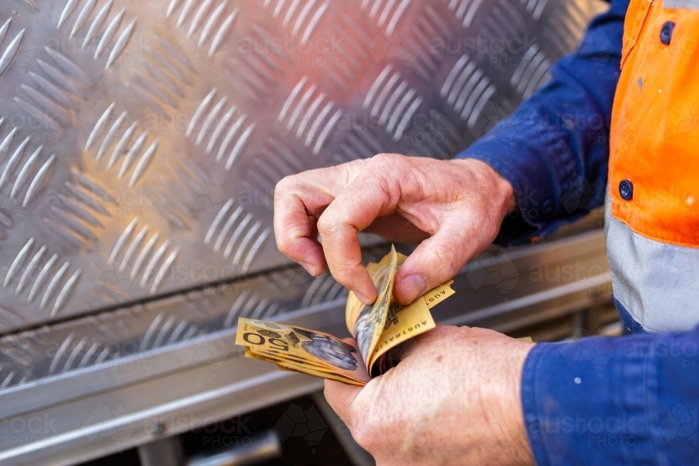 Hands of a handyman counting cash beside tradie ute - Australian Stock Image