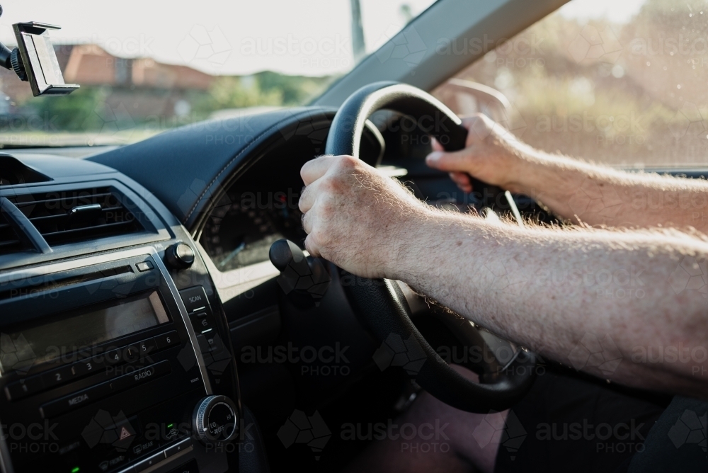 Hands of an anonymous male adult on the steering wheel seen from inside the car - Australian Stock Image