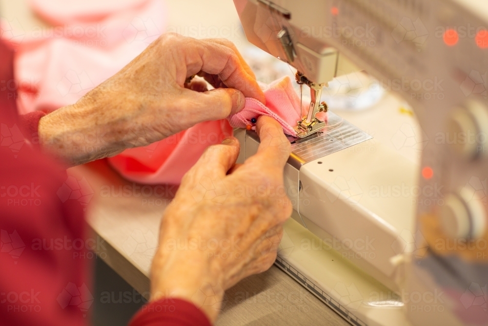 hands of elderly lady guiding fabric through sewing machine - Australian Stock Image
