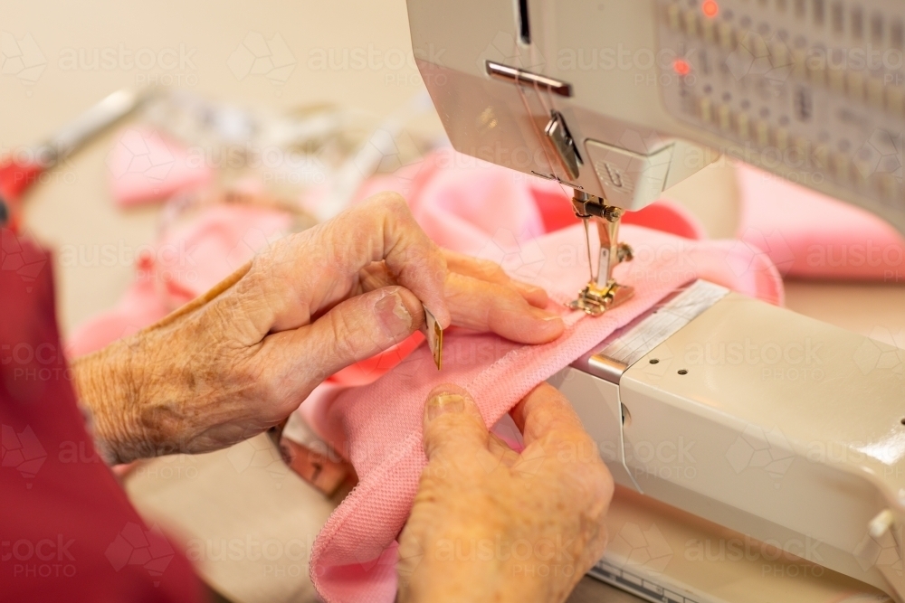 hands of elderly person guiding fabric on sewing machine - Australian Stock Image