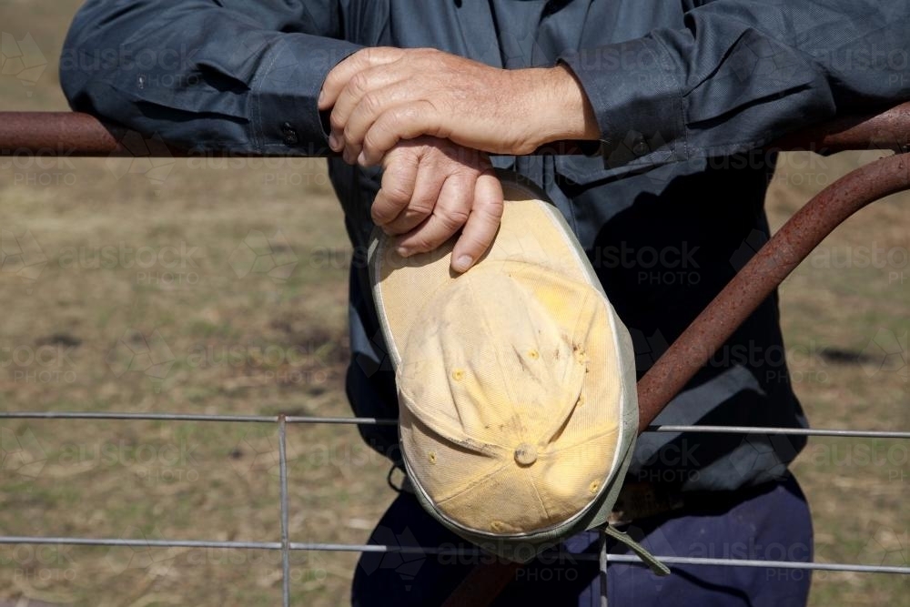 Hands of middle aged male farmer leaning on fence on rural property - Australian Stock Image