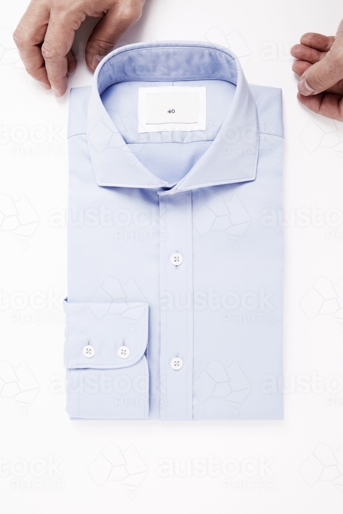 Hands styling blue tailored shirt on white background - Australian Stock Image