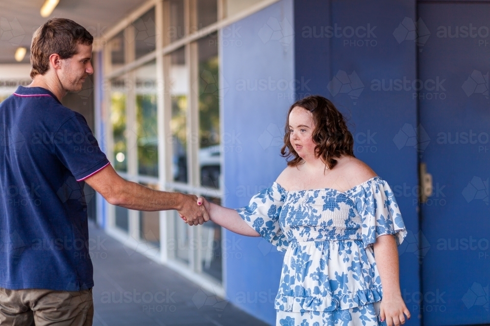 Handshake of congratulations between teen with down syndrome and support worker - Australian Stock Image