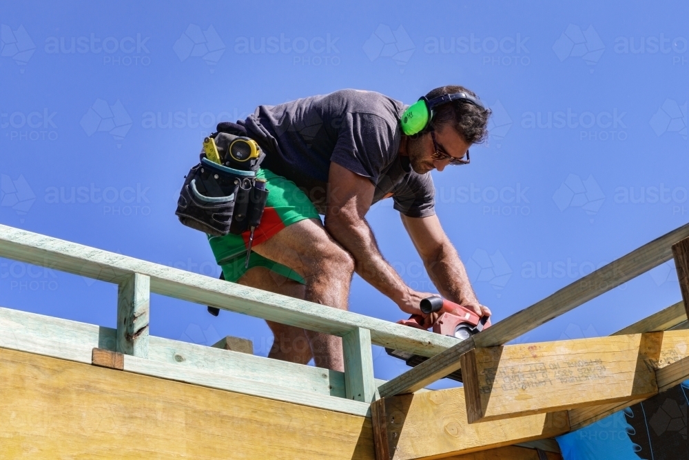 Handsome young builder working with circular saw on timber framing on building site - Australian Stock Image