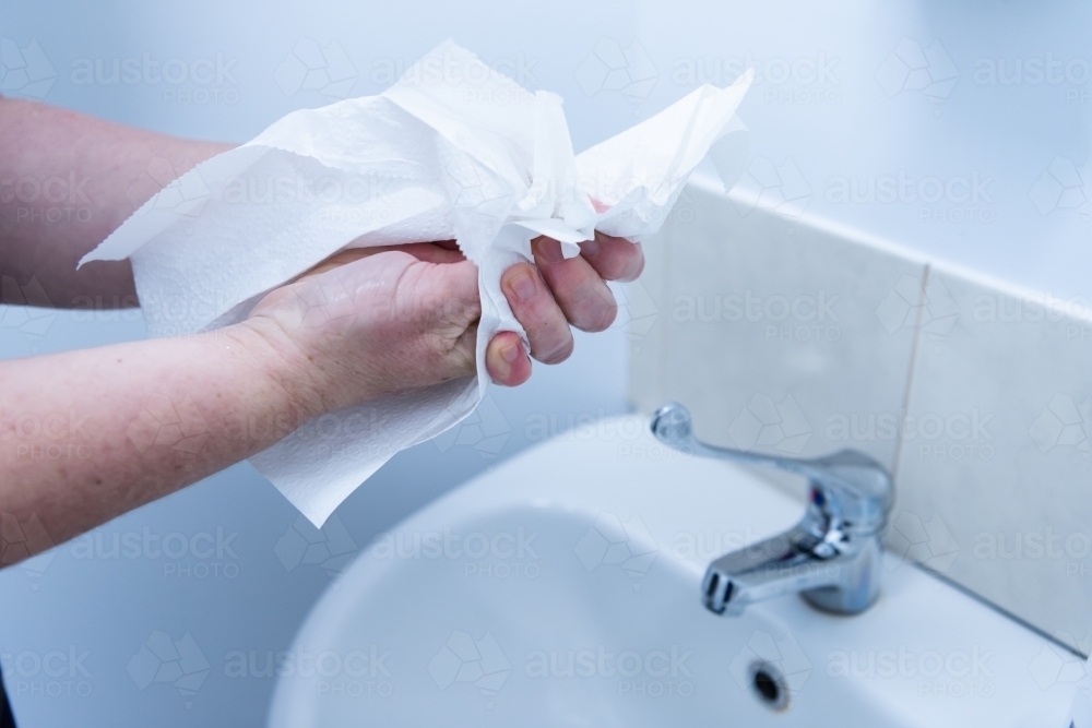 Handwashing - drying hands with paper towel after washing at basin - Australian Stock Image