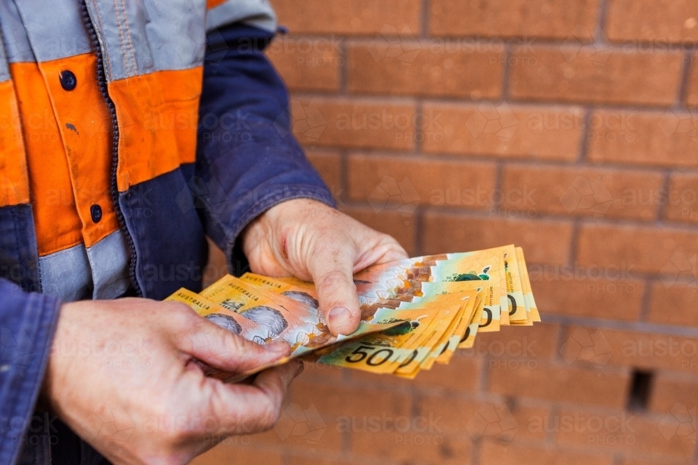 Handyman holding bank notes counting cash received as payment for job completion - Australian Stock Image