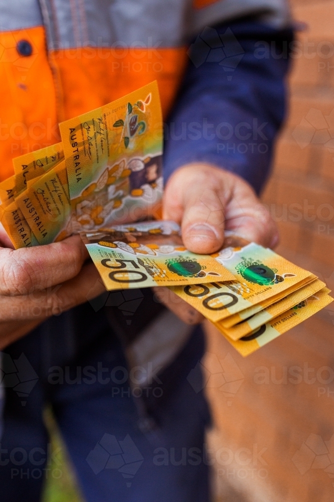 Handyman holding bank notes counting cash received as payment for job completion - Australian Stock Image