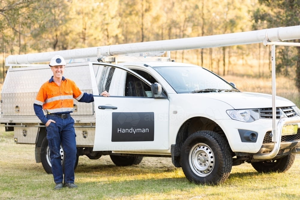 handyman with hard hat and high-vis workwear beside work ute - Australian Stock Image