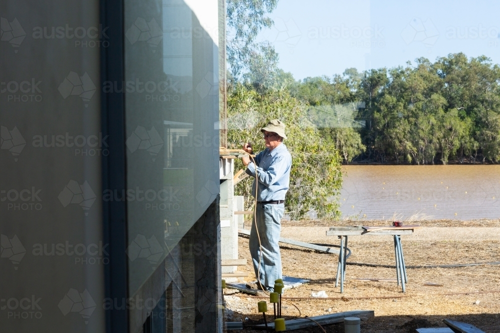 Handyman working outside seen through window - Australian Stock Image